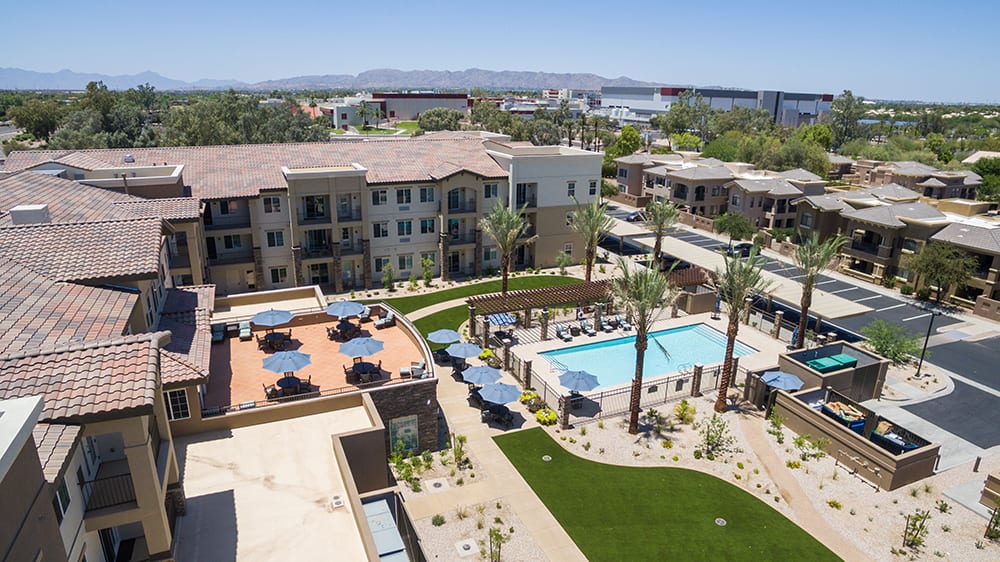 Aerial view of a modern apartment complex featuring a swimming pool and landscaped outdoor area with palm trees.
