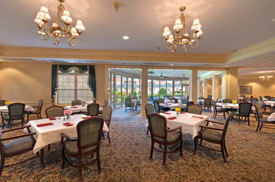 An elegant dining area with tables and chairs, adorned with chandeliers and large windows.