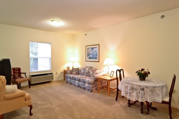 A cozy living room with a sofa, table, and lamps, featuring warm lighting and carpeted flooring.