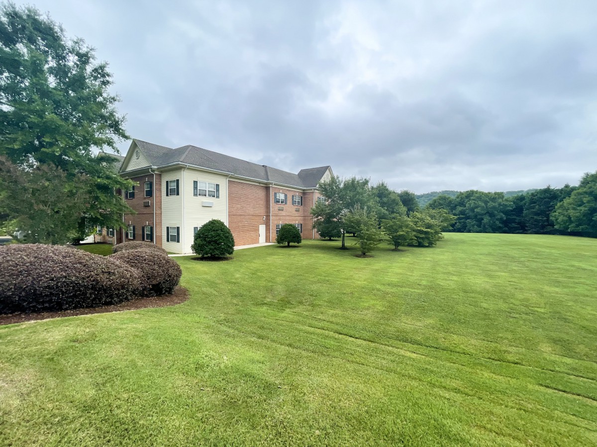 A residential building surrounded by a vast green lawn under an overcast sky.