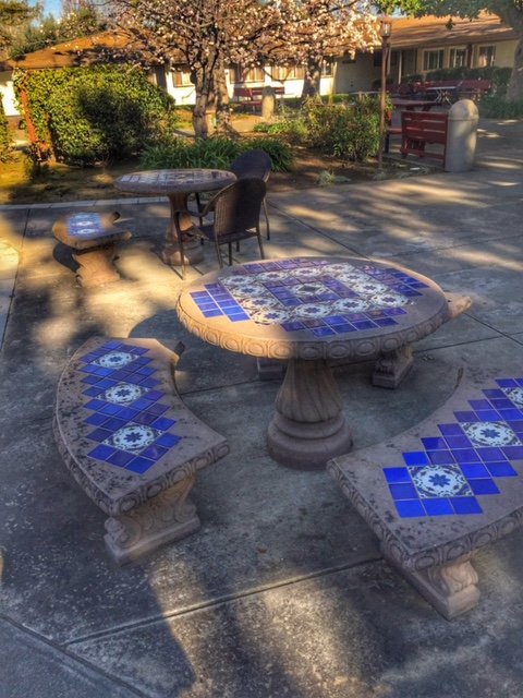 A decorative outdoor table and benches with blue mosaic patterns, set in a garden patio.