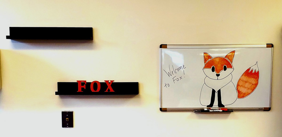 A wall with a decorative shelf and a whiteboard featuring artwork and writing.
