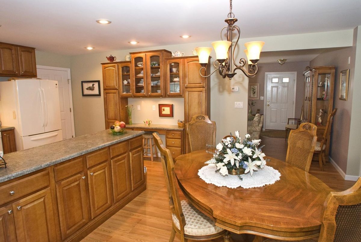 A cozy kitchen and dining area featuring wooden cabinets, a round dining table with a floral centerpiece, and a chandelier.