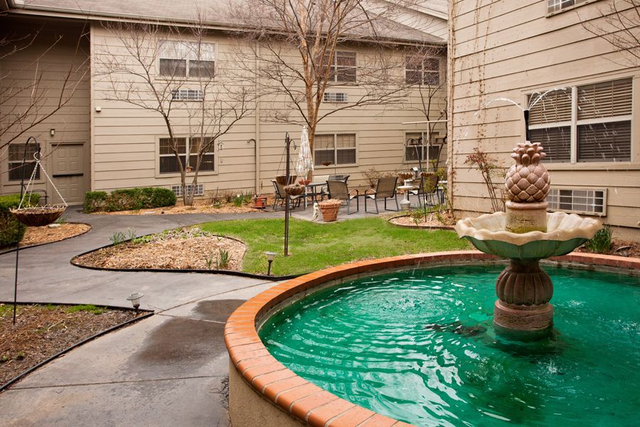 A serene courtyard featuring a central fountain surrounded by greenery and building structures.