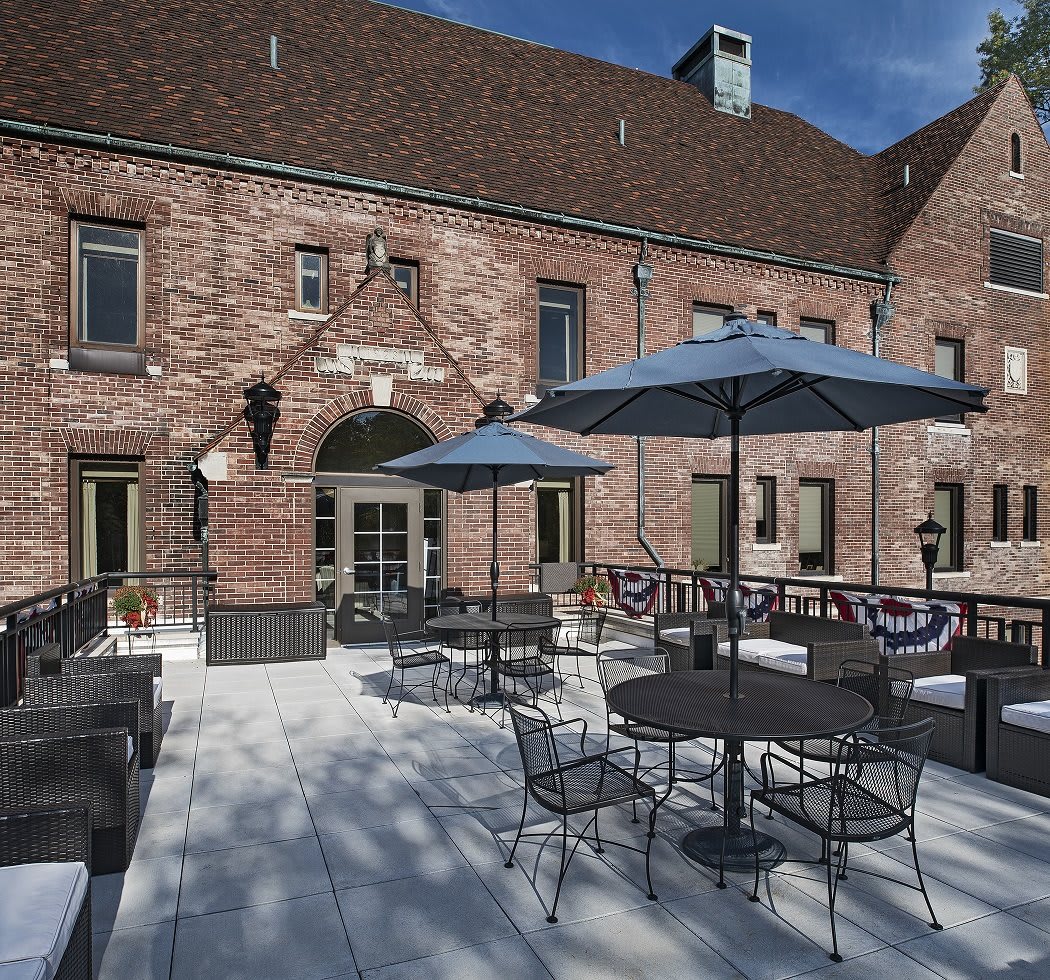 A sunny patio with tables, chairs, and umbrellas outside a brick building.