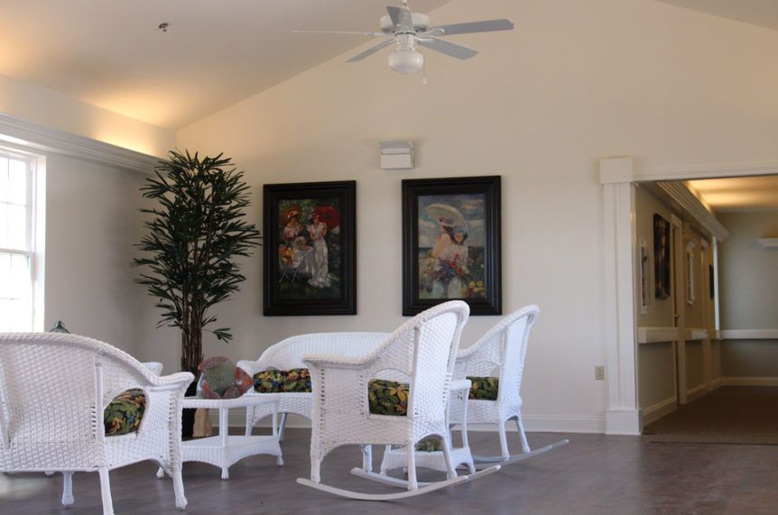 A cozy living room featuring white wicker furniture, an indoor plant, and framed artwork.