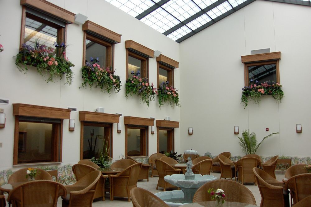 A spacious indoor atrium with a glass roof, featuring wooden seating and decorative plants.