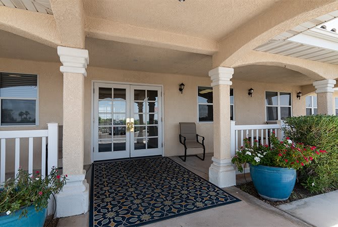 A welcoming entrance porch with columns, decorative rug, and potted plants.
