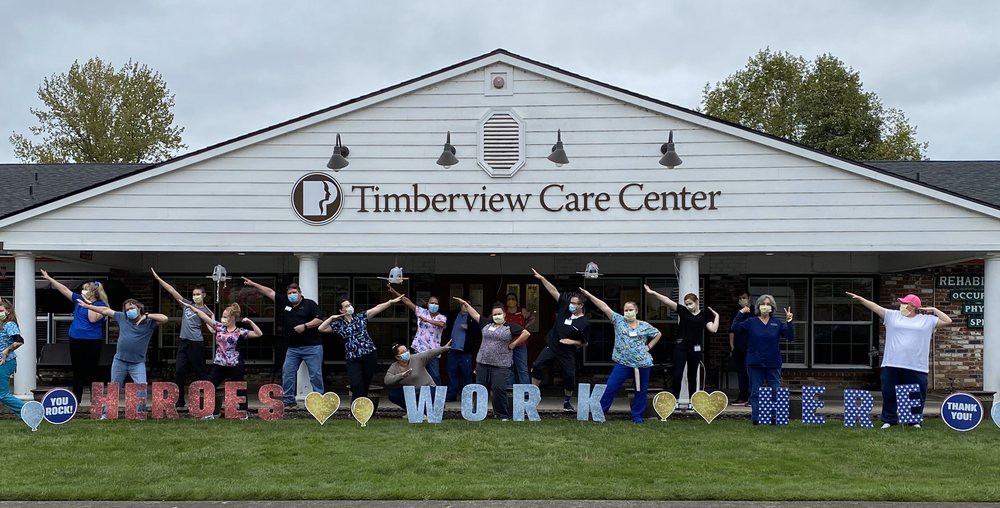 A group of people posing outside Timberview Care Center with cheerful signs.