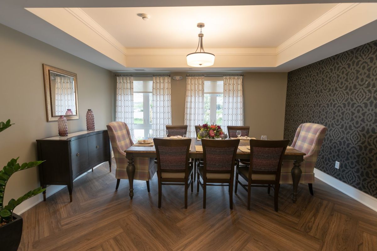 A spacious dining room with a large table, surrounded by elegant chairs and illuminated by a central chandelier.