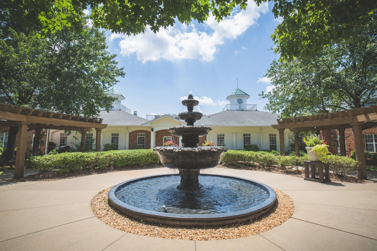 A beautiful outdoor fountain surrounded by greenery and architecture under a clear blue sky.