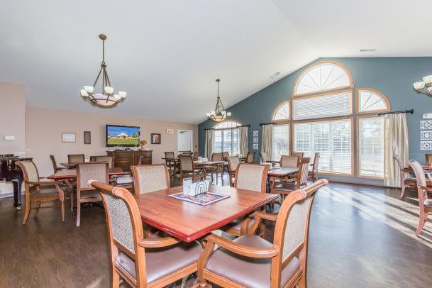 A spacious dining area with wooden tables and chairs, illuminated by chandeliers and abundant natural light from large windows.