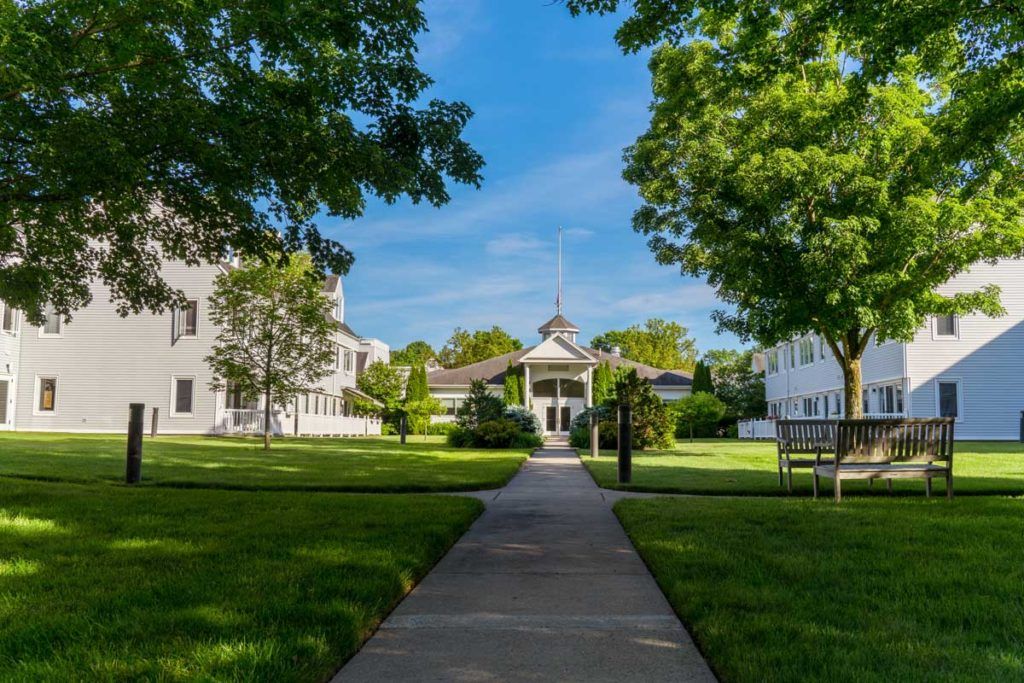 A path leading to a building surrounded by trees and greenery on a sunny day.