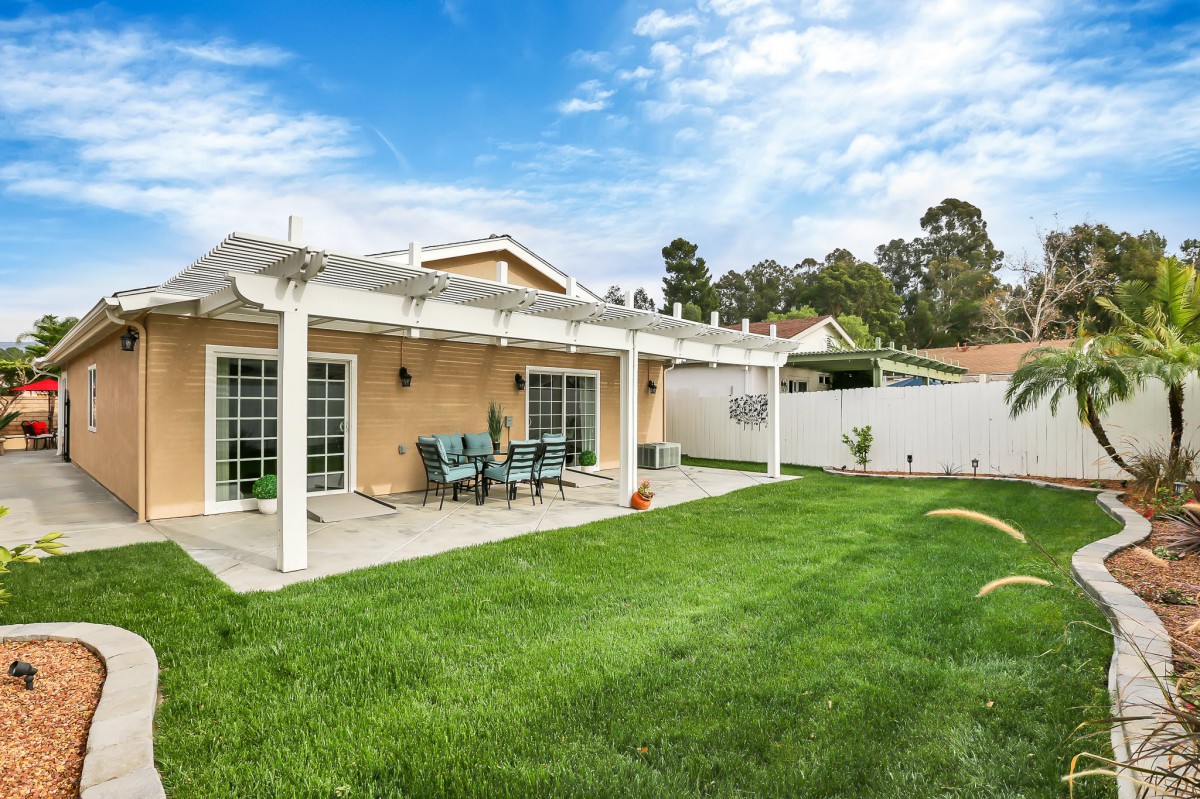 A backyard patio with a pergola overlooking a neatly maintained lawn and outdoor seating.