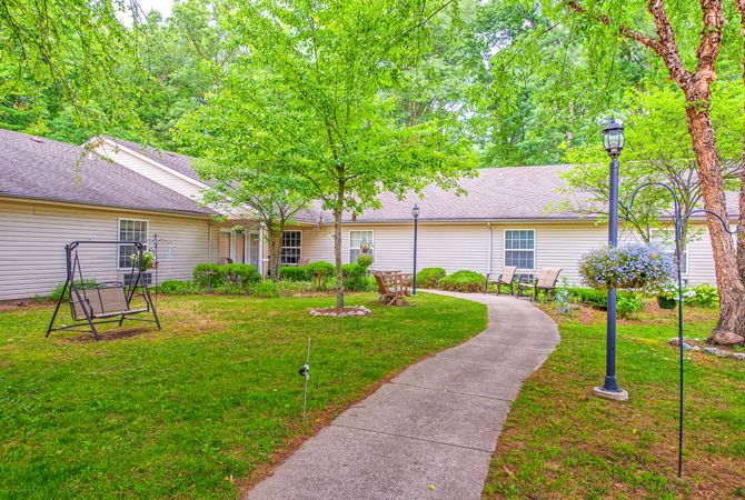 A peaceful garden with a pathway leading to a building surrounded by lush greenery.