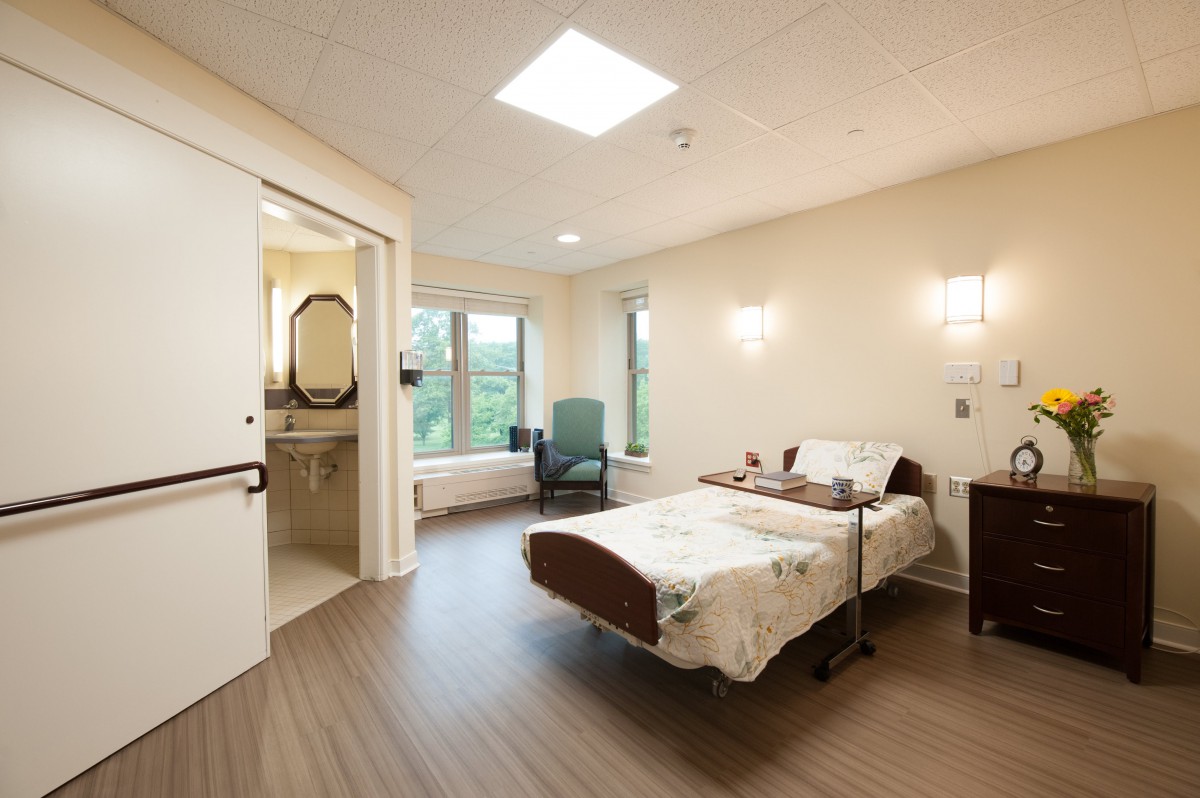 A spacious hospital room featuring a single bed, large window, and accessible bathroom.
