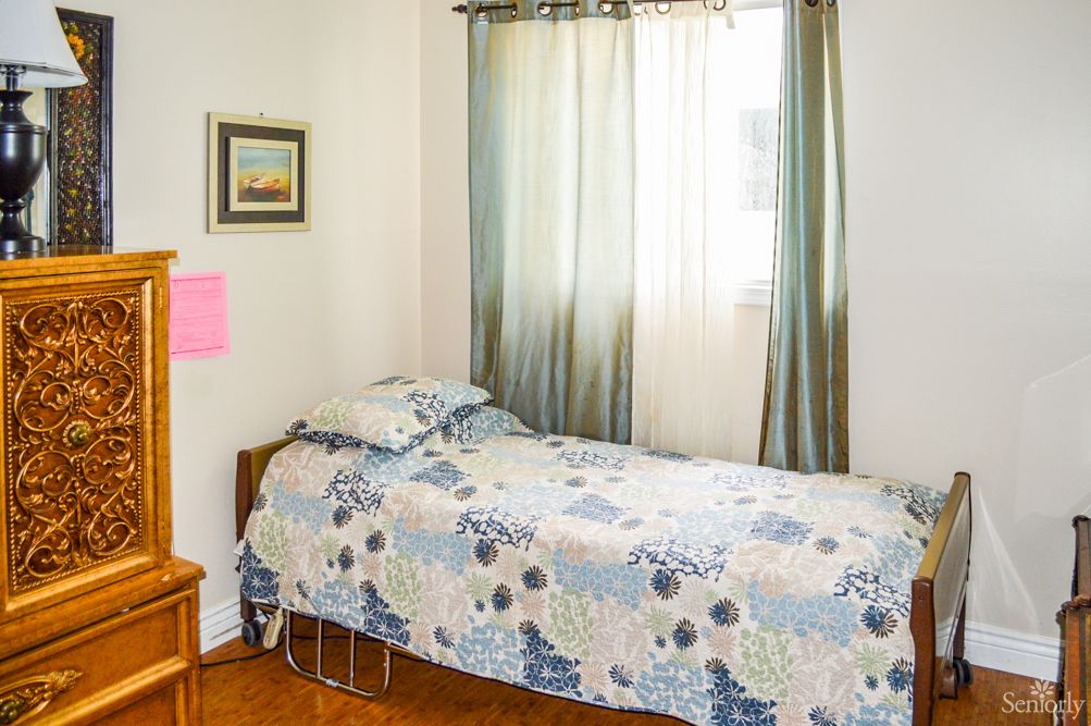A cozy bedroom with a single bed and floral bedspread near a window adorned with curtains.
