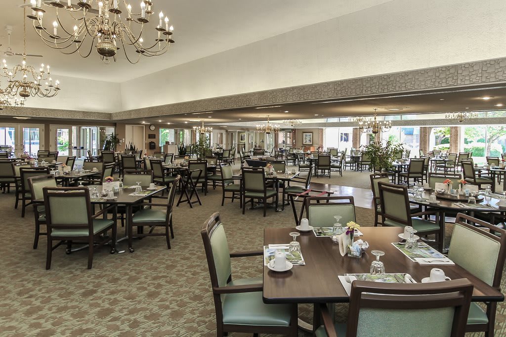 An elegant dining room with neatly arranged tables and chairs under chandeliers.