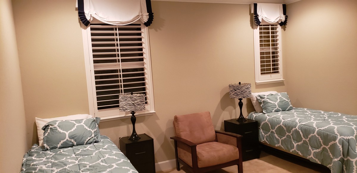 A cozy bedroom with a chair, twin beds, and lamps beside shuttered windows.