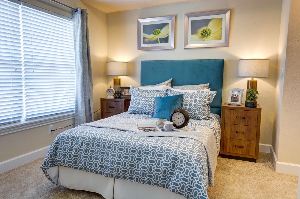 A cozy and stylishly decorated bedroom with a patterned comforter, pillows, bedside tables, and wall art.