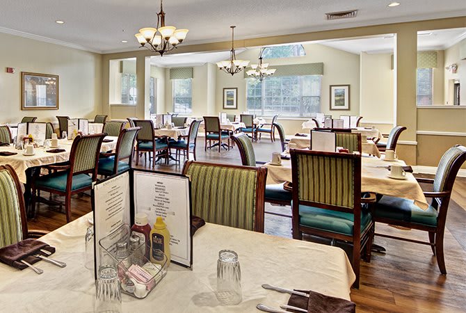 A spacious dining area with neatly arranged tables and chairs, featuring elegant lighting and menus displayed on the tables.