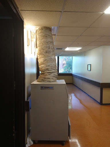 A unique ventilation tube decorated with what appears to be fabric or paper, positioned in an office hallway.