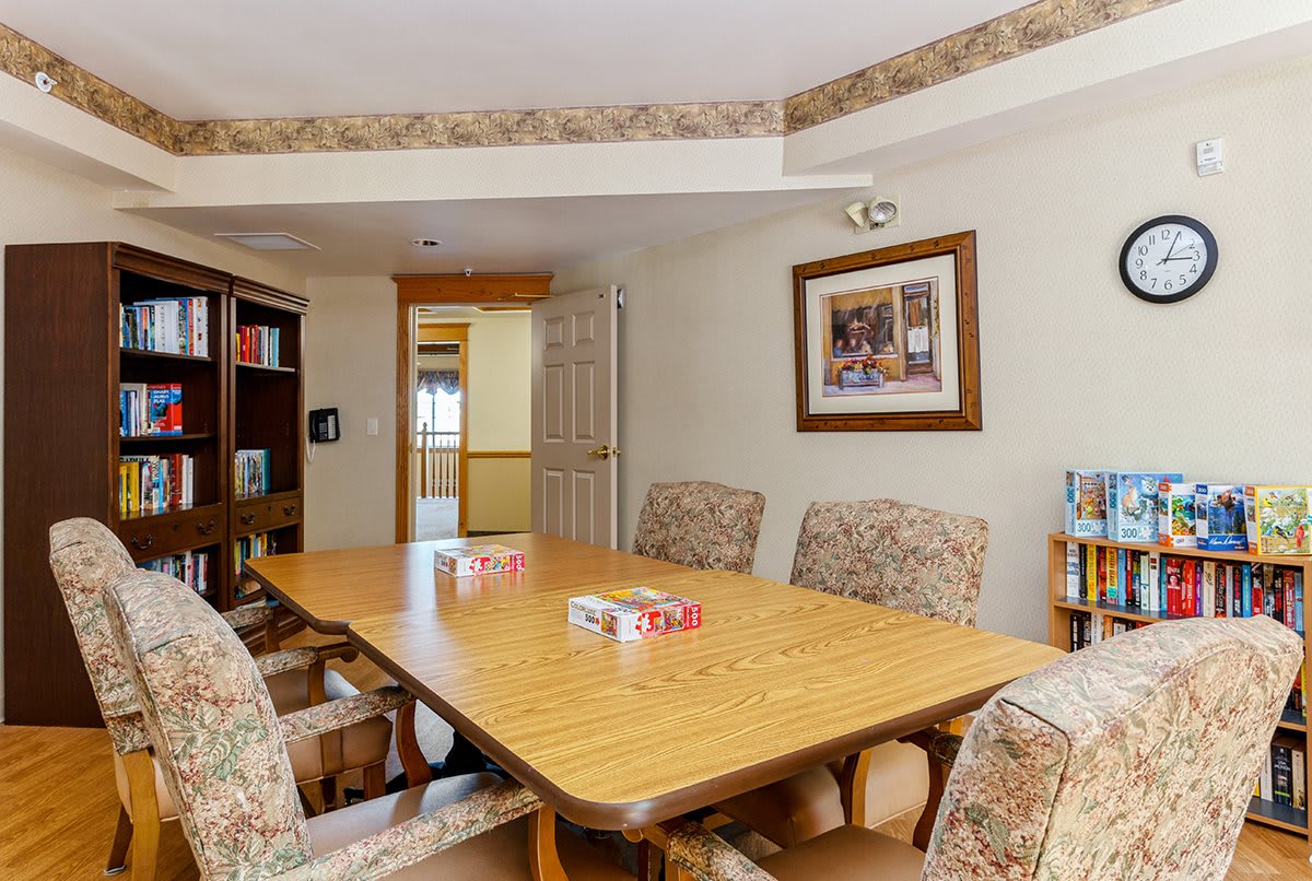 A cozy meeting room with a large conference table, surrounded by upholstered chairs and a bookshelf in the corner.
