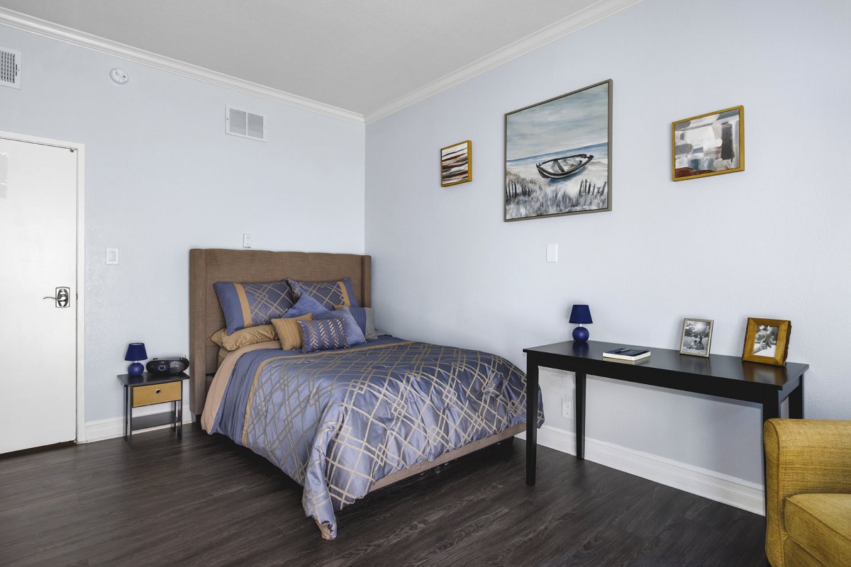 A cozy bedroom with a bed, a side table, and framed artwork on the walls.