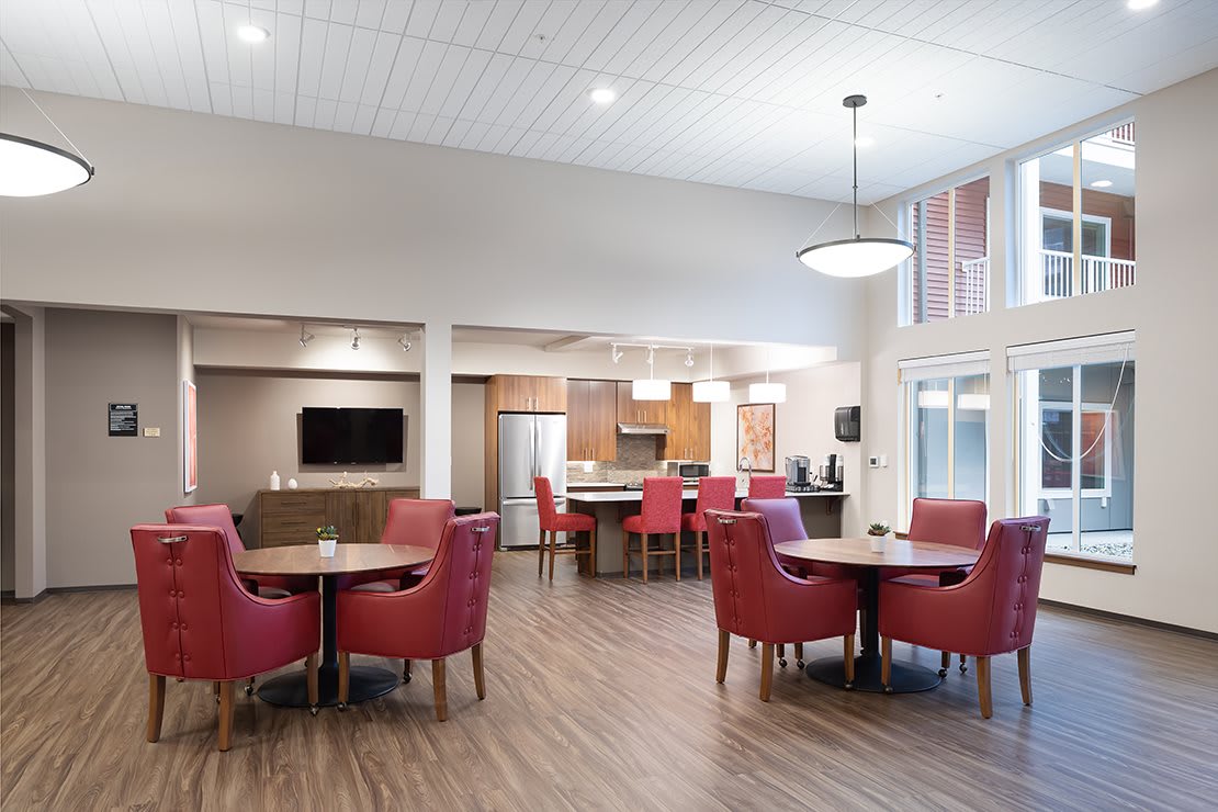 A modern dining and kitchen area with red chairs and wood flooring.