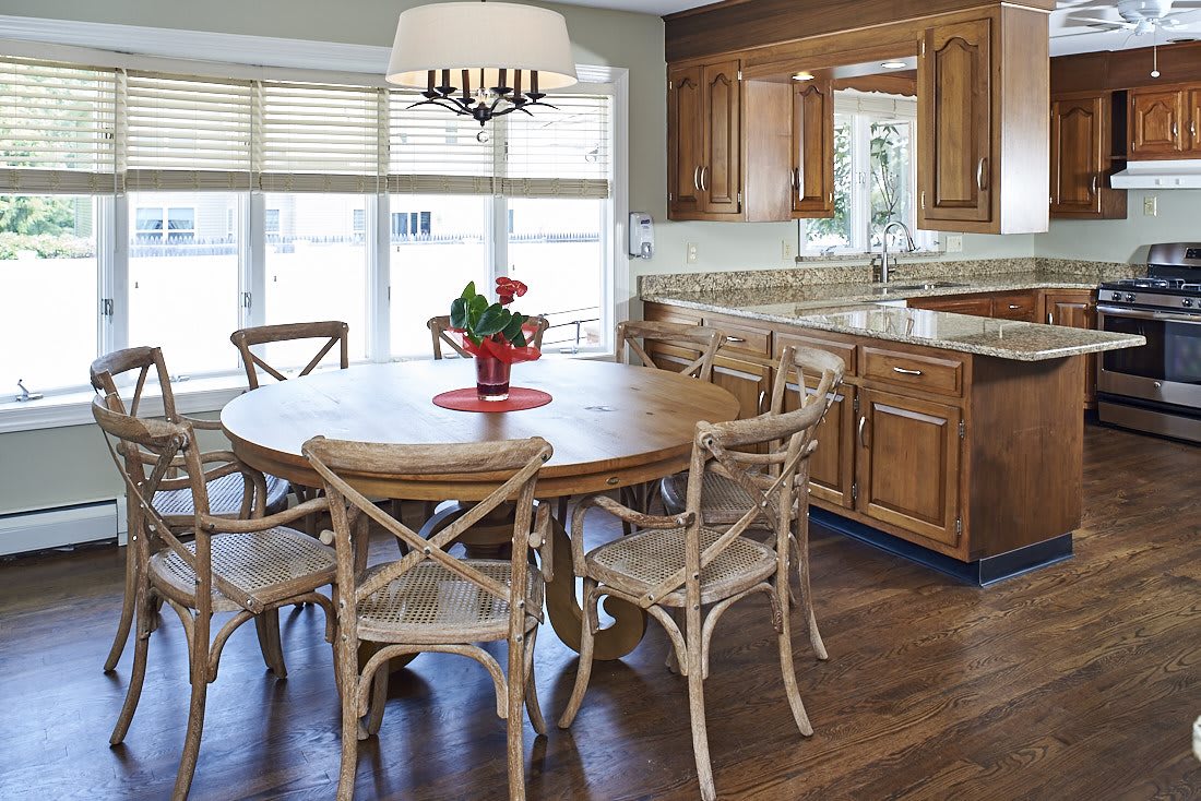 A cozy kitchen and dining area with a round wooden table and elegant chairs, complemented by warm wood cabinetry and modern lighting.