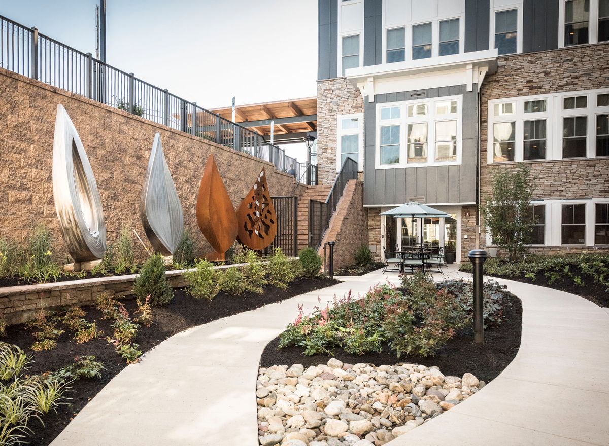 A modern garden with unique sculptures and a winding pathway alongside a contemporary building.