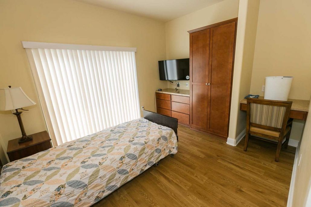 A cozy bedroom with a single bed, TV, dresser, and wooden flooring.