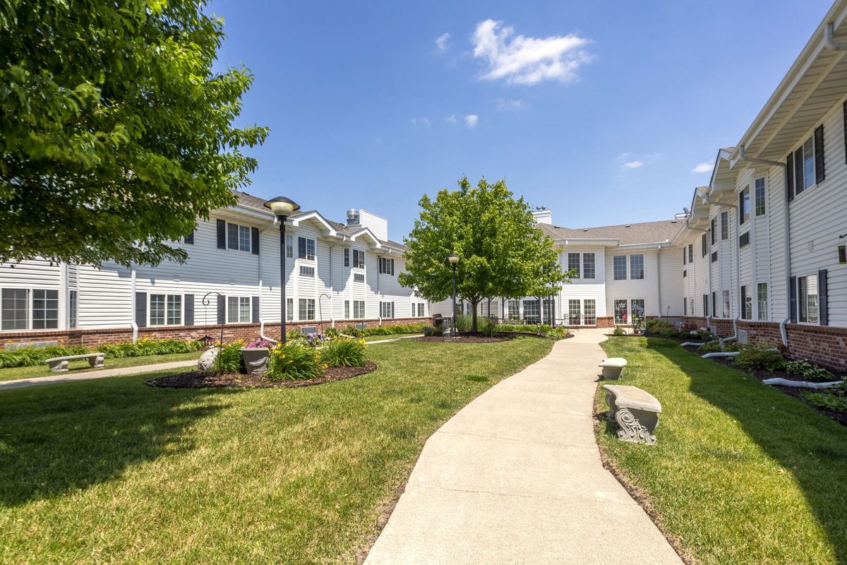A sunny day with a view of a building, surrounded by trees and a well-maintained lawn, alongside a winding pathway.