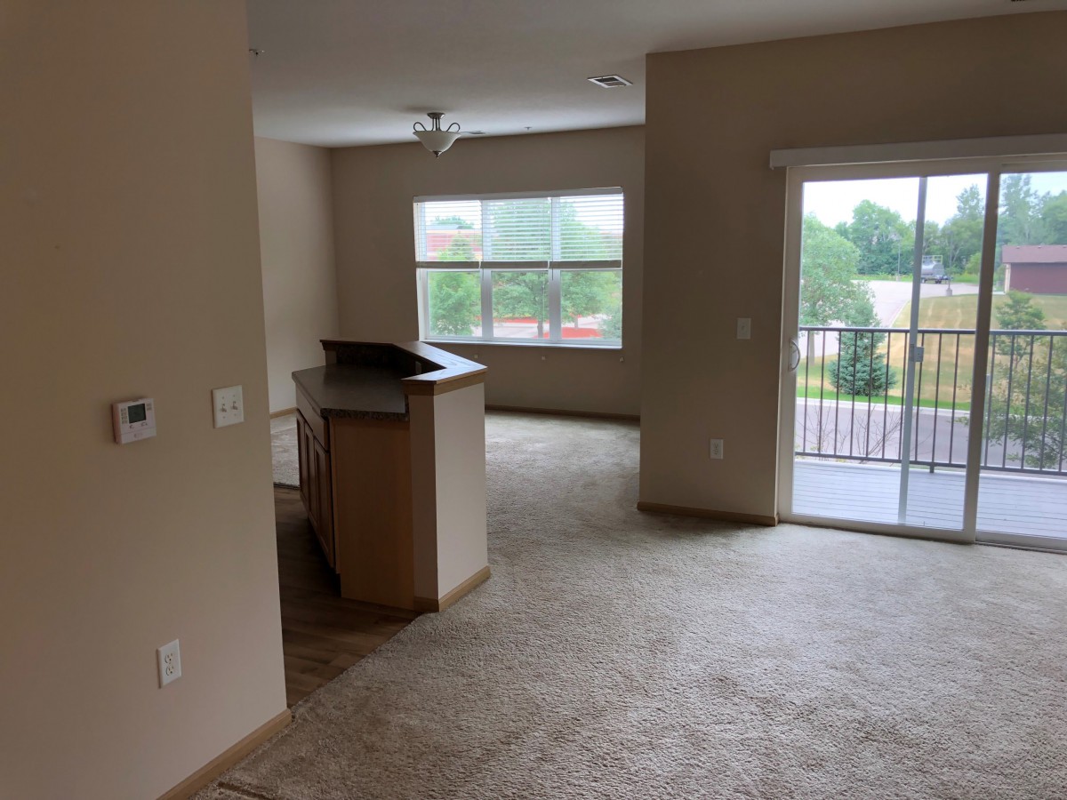 A spacious apartment living area with a view of the kitchen and balcony.