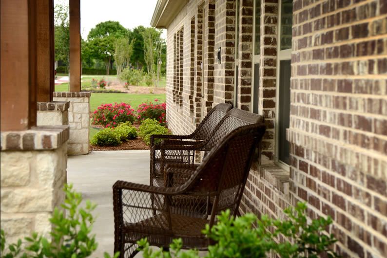 A cozy porch with wicker chairs facing a well-maintained garden.
