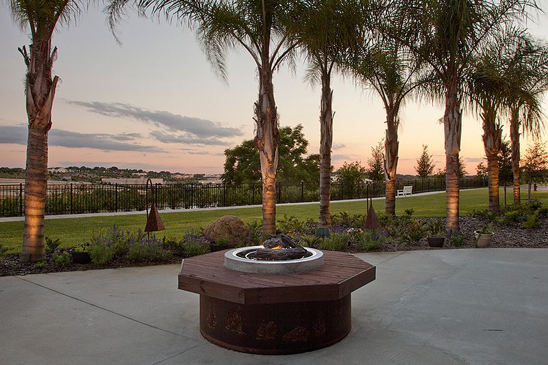 A serene outdoor patio featuring a fire pit surrounded by palm trees at sunset.