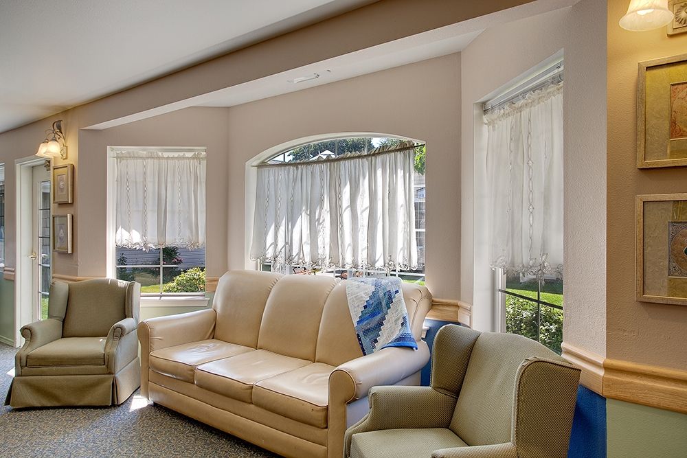 A cozy living room filled with natural light, featuring comfortable seating and large windows with sheer curtains.