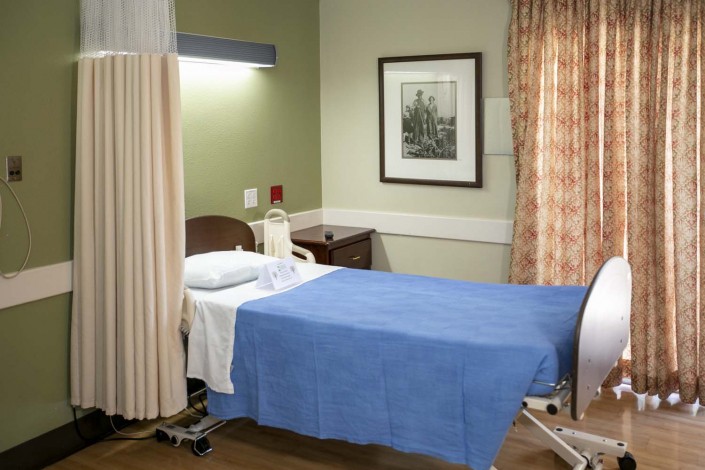 A clean and organized hospital room with a bed covered in a blue blanket, surrounded by curtains.