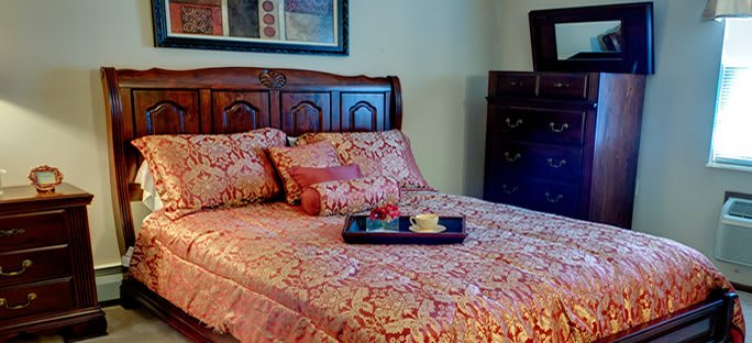 A cozy bedroom with a neatly made bed, featuring patterned bedding and a decorative tray with a drink on top.
