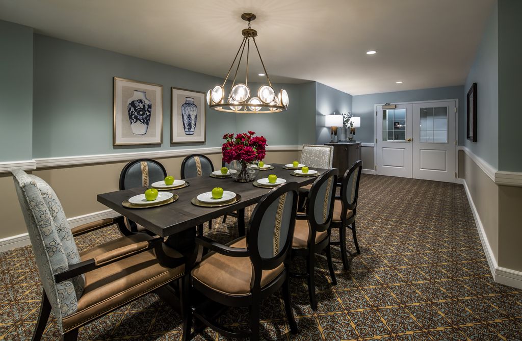 A stylish dining room with a large table set for four, featuring a chandelier and framed artwork on the walls.
