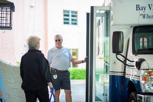 A conversation taking place at a bus stop, with an older woman speaking to a man standing at the bus door.