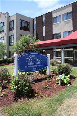 Entrance of The Pines at Pinecrest featuring a landscaped sign and modern building.