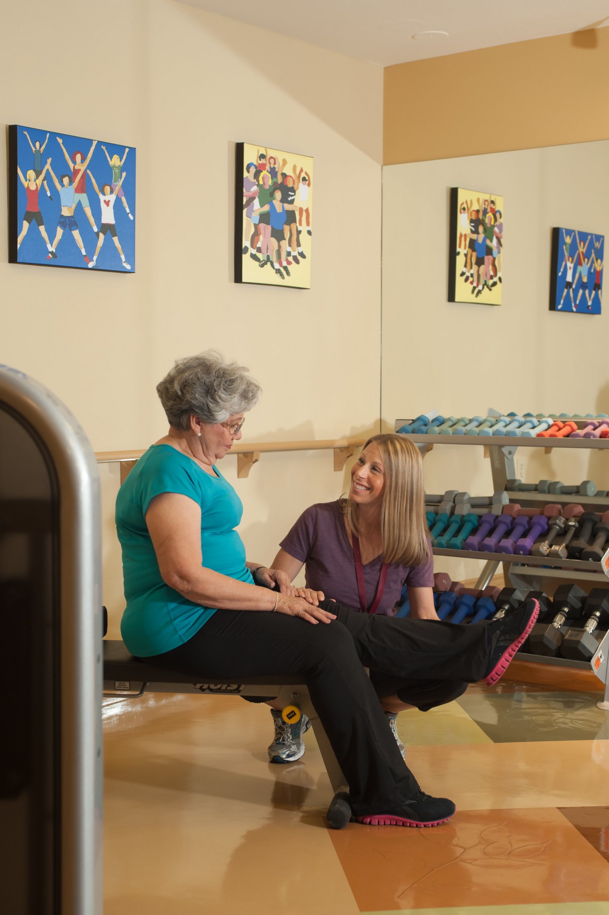 Two women engaging in a fitness session at the gym, with weights visible in the background.