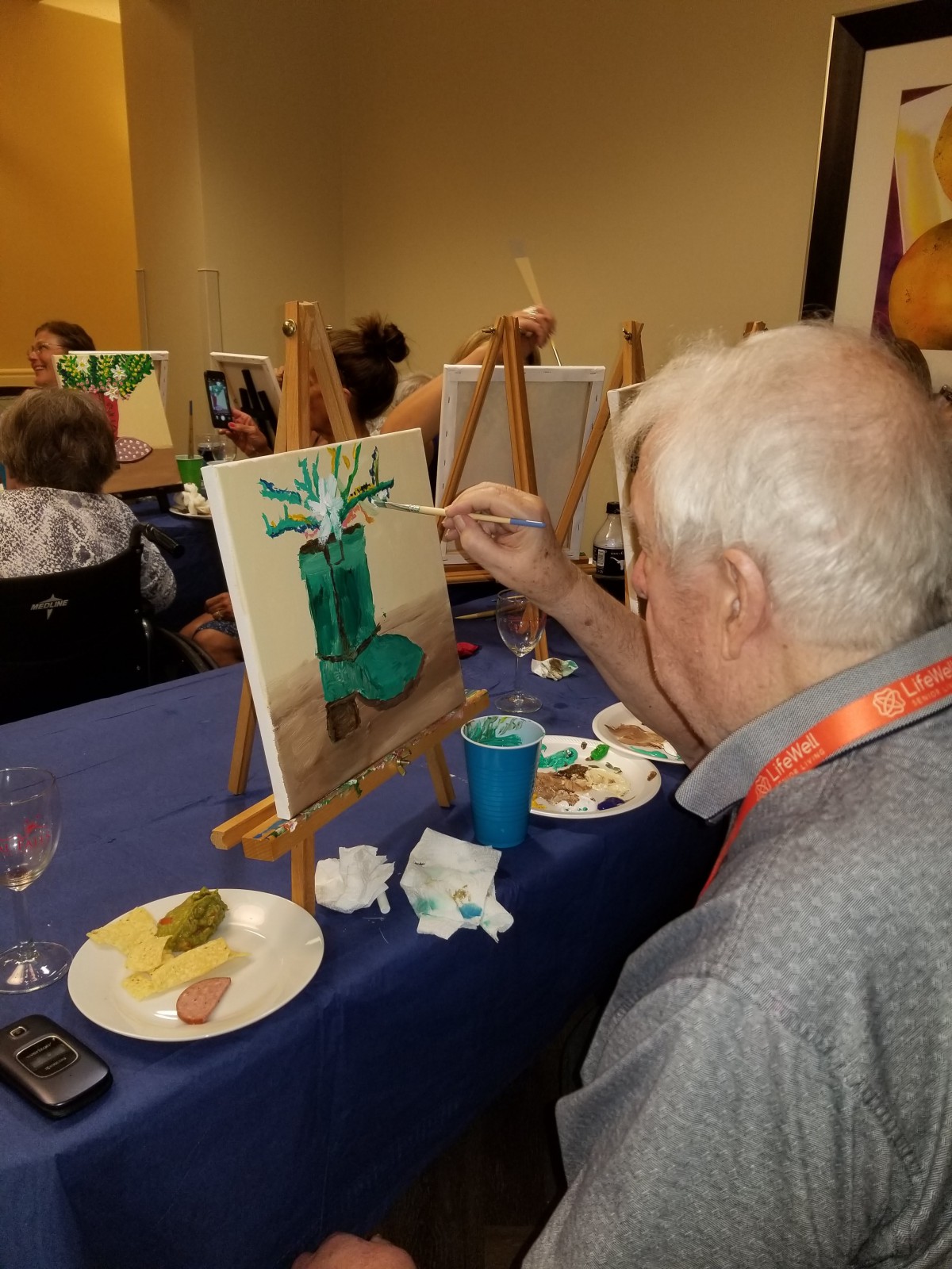 A senior man participating in an art class, painting on a canvas at an easel.