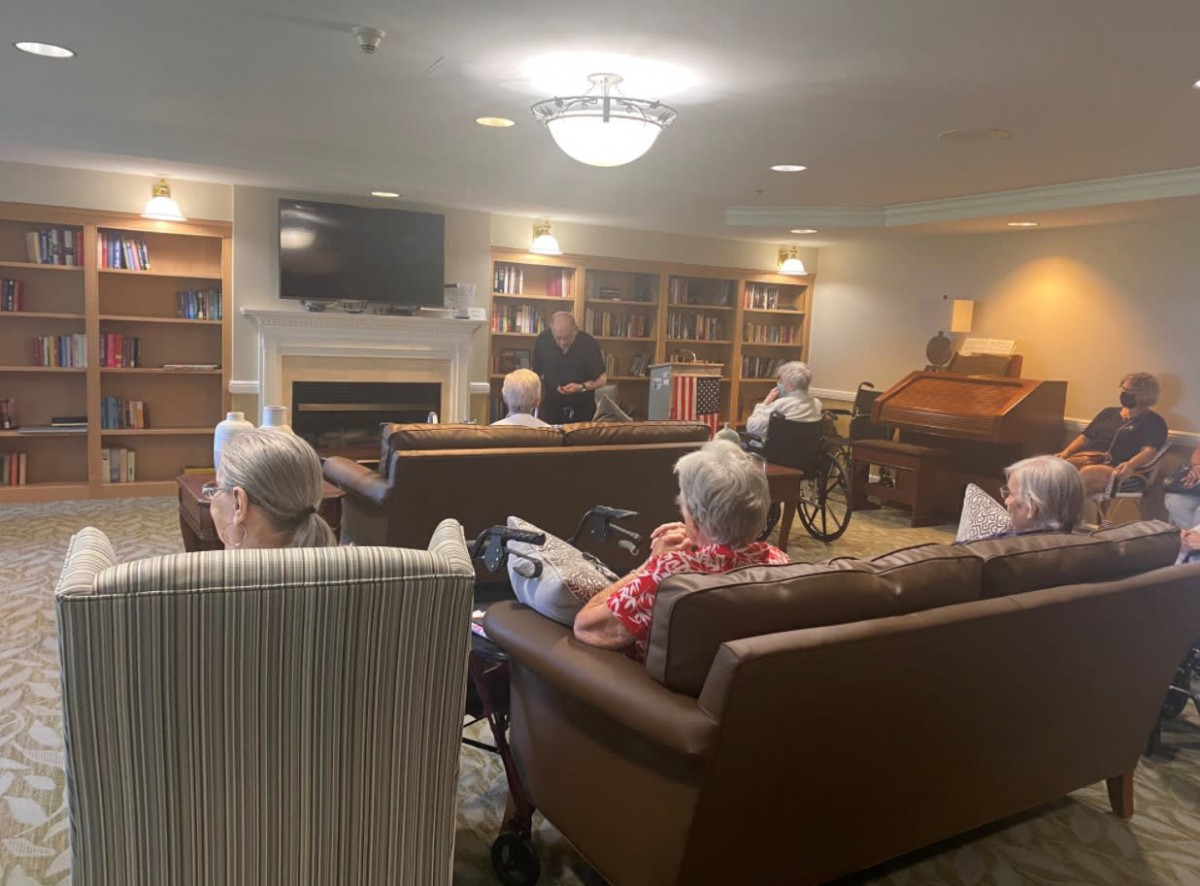 A group of elderly individuals sitting in a cozy library at a retirement home, engaging in conversation and activities.