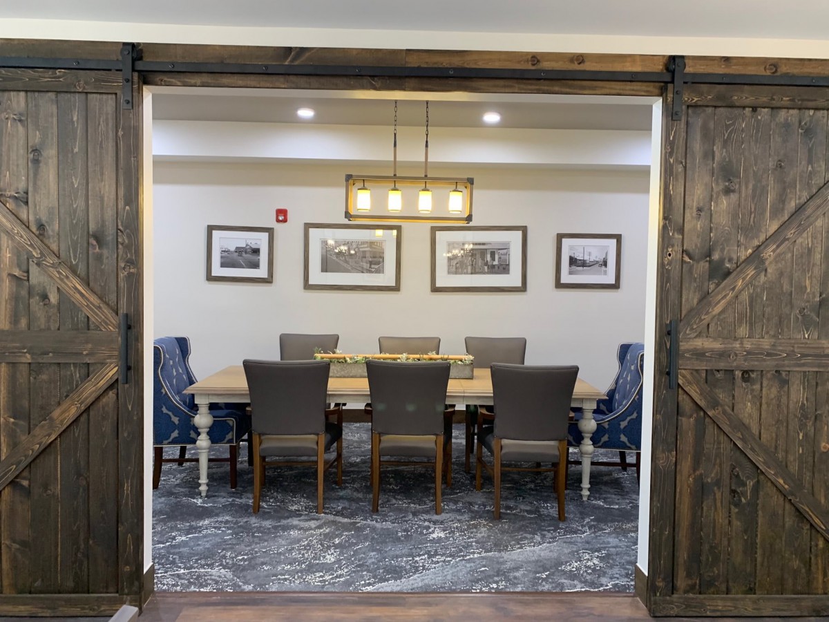 A well-decorated dining or meeting room with a large wooden table, surrounding chairs, stylish lighting, and framed artwork on the walls.
