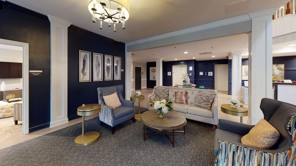 A cozy living room with modern decor, featuring a sofa and armchair, accented by a chandelier.