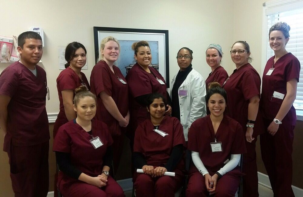 A group of medical staff members posing together in a hospital setting, wearing matching maroon scrubs and one in a white coat.
