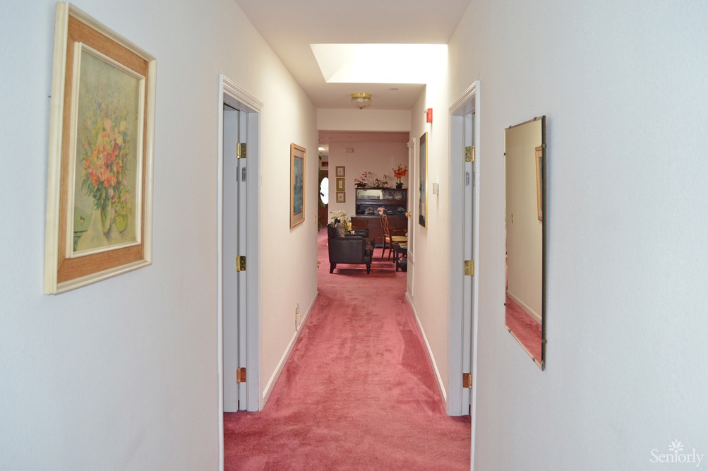 A hallway with red carpet, featuring several doors and decorated with artwork on the walls.