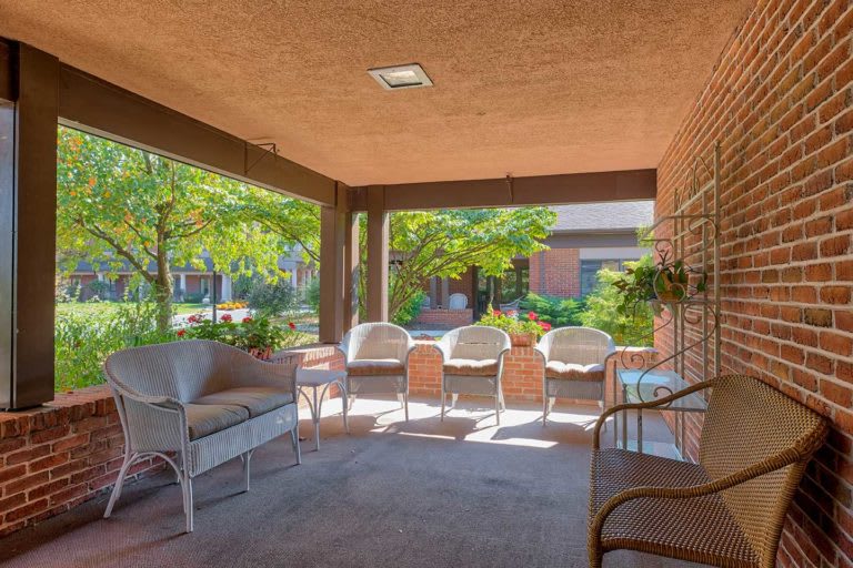 A shaded outdoor patio with seating surrounded by greenery.